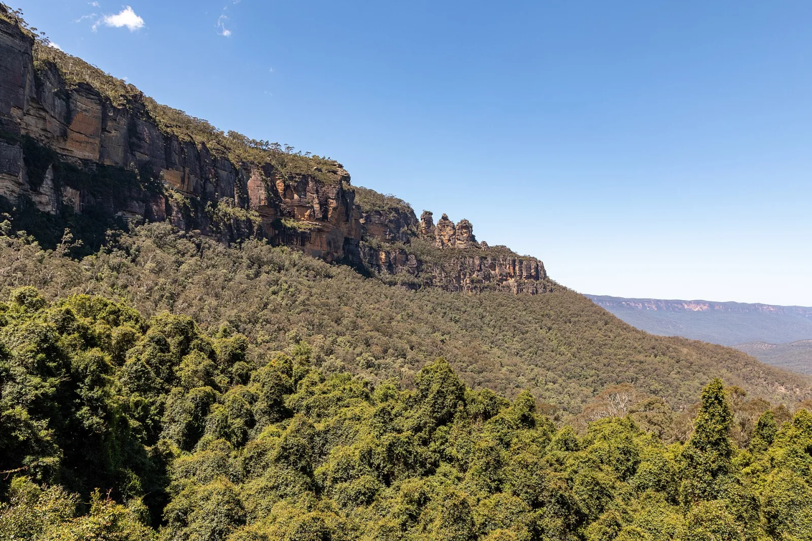 Three Sisters, Blue Mountains National Park, New South Wales, AustraliaThe Blue Mountains National Park is located west of Sydney and is one of Australia’s most famous natural areas. Its history is closely linked to Aboriginal culture, particularly that of the Gundungurra and Darug peoples, who have inhabited the area for tens of thousands of years and have a spiritual connection to the landscape.For European settlers, the rugged sandstone plateaus were long considered an insurmountable obstacle. It was not until 1813 that Gregory Blaxland, William Lawson, and William Charles Wentworth succeeded in crossing the mountains, opening the way for the development of the Australian hinterland.In the 19th century, parts of the region were used for logging and mining, while at the same time its scenic appeal was discovered. In 1959, the Blue Mountains National Park was officially established to protect the unique eucalyptus vegetation, deep gorges, and waterfalls.In 2000, UNESCO declared the area part of the Greater Blue Mountains Area a World Heritage Site. Today, the park stands for nature conservation, tourism, and recognition of Australia’s indigenous cultural history.