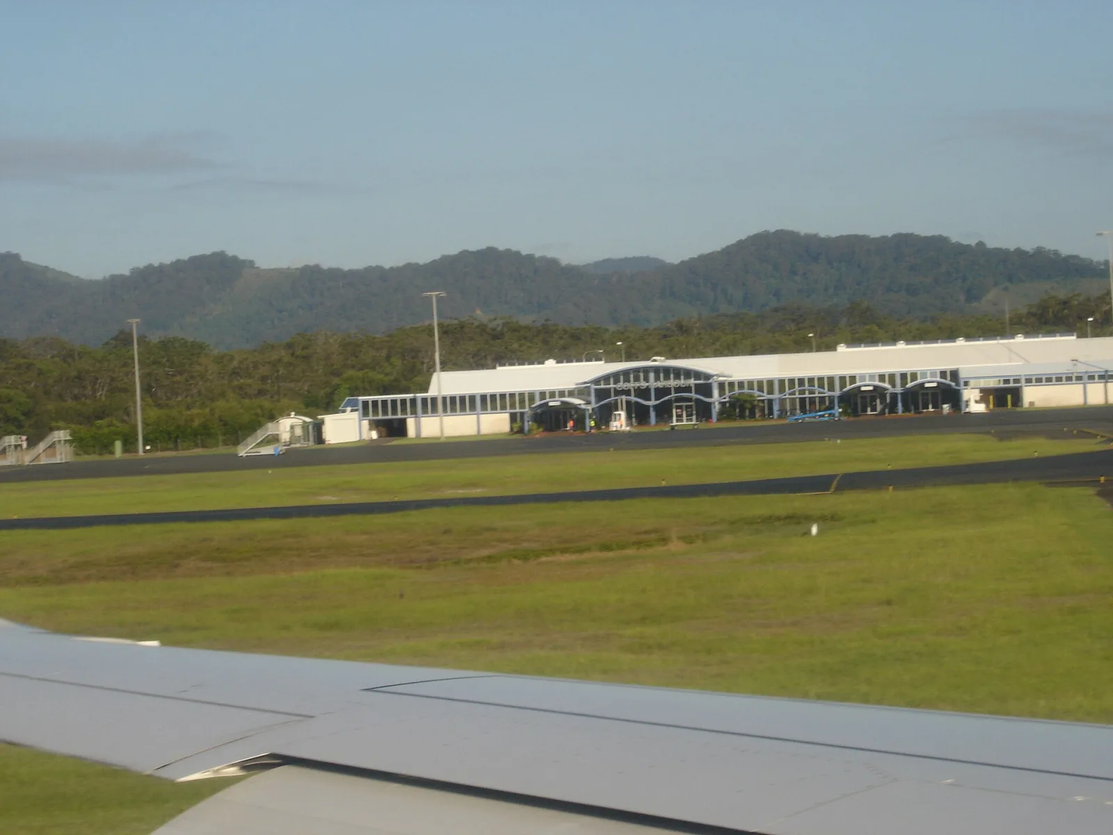 The image is of the Coffs Harbour airport terminal taken from the runway on an arriving aircraft. The door to the far left is for arrivals, with the other two doors being gates for departures.